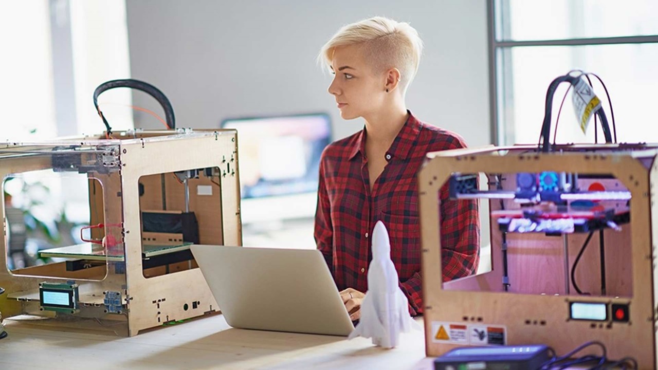Junge Frau mit Laptop zwischen zwei 3D-Drucker
